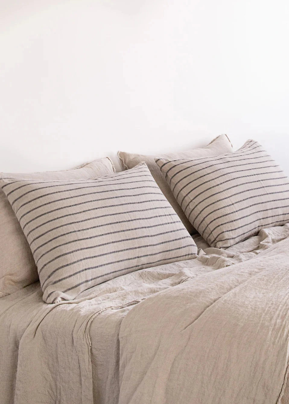 Neatly made bed with beige bedding and striped pillows against a white wall.
