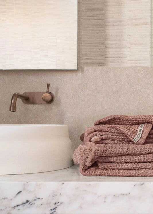 Folded pink towel on a marble countertop with a neutral bathroom background